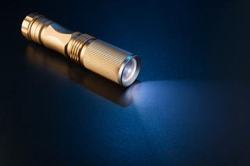 Working flashlight on a blue surface. - obrazy, fototapety, plakaty