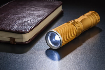 Luminous flashlight on a dark surface. Notepad in the background ..