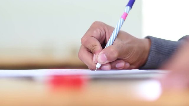 Asian student boy hands writing on paperwork or homework during test exam in classroom