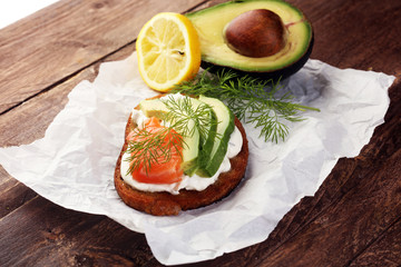 Bread with avocado and smoked salmon for lunch table. Sharing antipasti on party or summer picnic time over wooden rustic background.