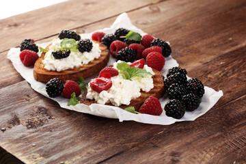 Bread with cheese cream and blackberries and raspberries for lunch table. Sharing antipasti on party or summer picnic time over wooden rustic background.