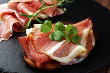 Bread with slices jamon serrano for lunch table. Sharing antipasti on party or summer picnic time over wooden rustic background.