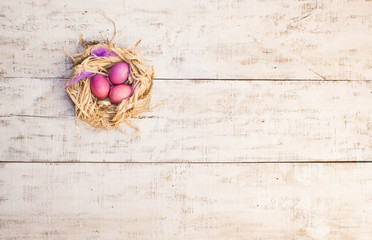 Easter eggs in nest, bird feathers on white wooden background.