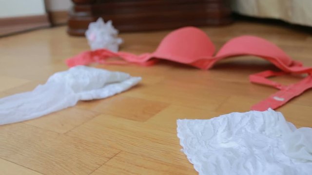White and pink sexy underwear lying on the floor next to the bed
