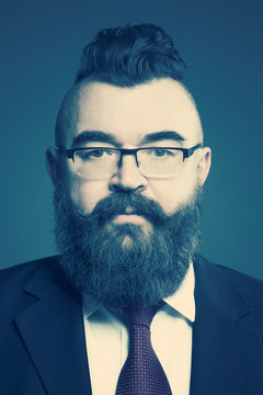 Adult bearded man in a suit, glasses and a mohawk hairstyle on a blue background