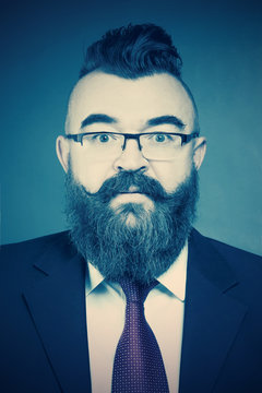 Adult bearded man in a suit, glasses and a mohawk hairstyle on a blue background. Toned