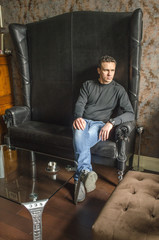 Sitting man in a black sweater and blue jeans on a black leather sofa