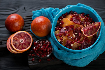 Bowl with blood oranges and pomegranate fruit salad over black wooden background