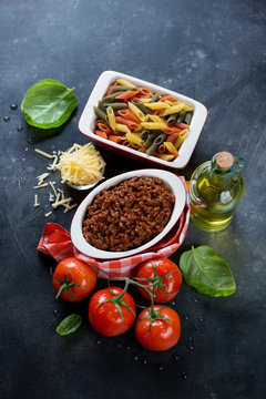 Bolognese sauce with raw penne tricolore and other italian cooking components, high angle view