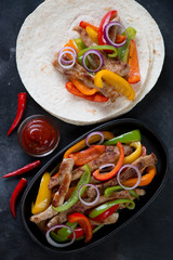 Cast-iron frying pan and tortillas with mexican pork fajitas, high angle view, studio shot