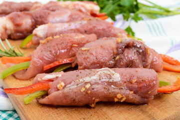 Un-cooked, pork meat rolls stuffed with vegetables (pepper, carrots) in hot garlic sauce on a cutting board. Raw, semi-finished product.