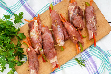 Un-cooked, pork meat rolls stuffed with vegetables (pepper, carrots) in hot garlic sauce on a cutting board. Raw, semi-finished product. The top view