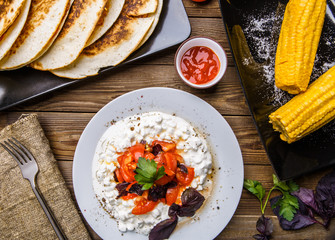 Quesadilla, salad with cottage cheese and tomatoes, two corn on wood table.