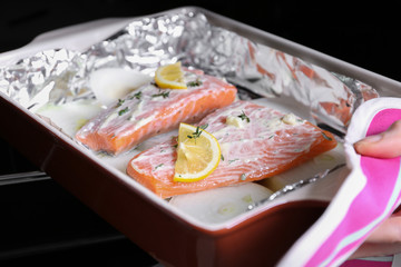 Hand putting baking dish with delicious salmon fillet into oven