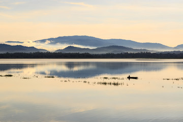 small fishing boat in lake with foggy over mountain background and reflection in the pond
