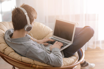 Teenager working with laptop while listening to music at home