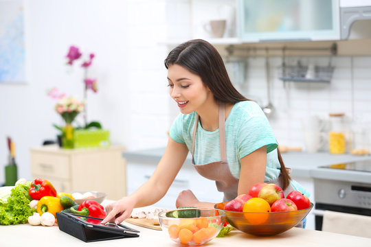 Beautiful young woman with tablet computer in kitchen