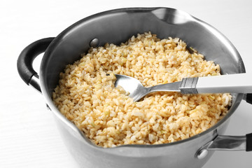 Pan with boiled brown rice on white background