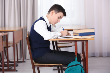 Incorrect posture concept. Schoolboy sitting at desk in classroom