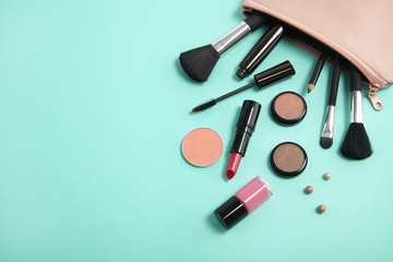 Make up products spilling out of a pastel pink cosmetics bag on to a turquoise background, with blank space at side