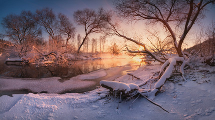 Beautiful calm evening on the small winter river, surrounded by overhanging trees. The last rays of...