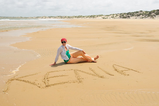 Tourist sitting on beautiful beaches of the Lamu archipelago with the Kenya inscription on sand