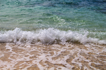 Sea with white wave splashing over beach. Waving sea. Clear turquoise blue sea water over sand beach.