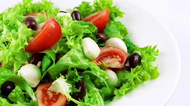Edge of plate with vitamin and gluten free salad with mozzarella, pine nuts, lettuce leaf, tomatoes and olives, loop
