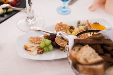 Appetizing food into the white plate on a banquet table: grape, cheese, nuts, snacks.