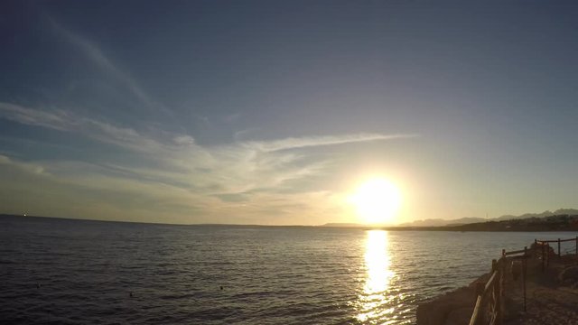 The sun at sunset reflects in the sea. On the horizon there are mountains