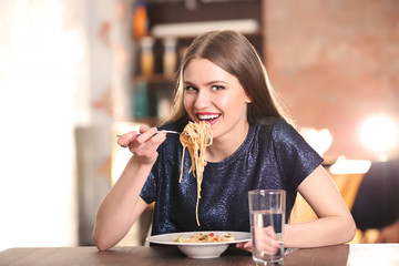 Beautiful woman eating pasta on table against blurred background