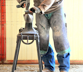 Male farrier working on a horseshoe inside a stable.