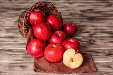 Wicker basket with fresh red apples on wooden background