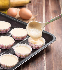 Pouring banana cake into preparing cupcakes.