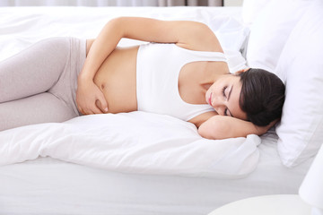 Beautiful pregnant woman touching her belly lying on bed at home