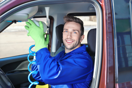 Handsome male cleaner removing dirt from car salon