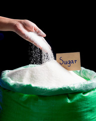 Sugar being poured from hand into bag of sugar on dark background