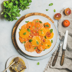 Fresh mixed citrus fruit salad with mint and honey on white ceramic plate over grey background, top view, square crop. Vegan, vegetarian, healthy, dieting, detox food, clean eating concept