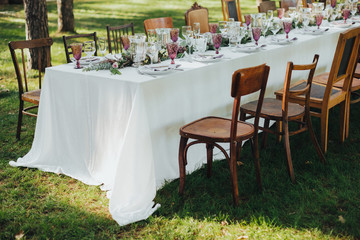 Festive table served dishes and decorated with branches of greenery, stands on green grass in the area of wedding party