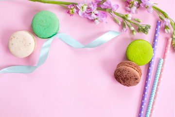 Multicolored macaroons сakes, straws for juice and flowers on a pink background.