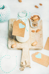 Fresh vegan dairy-free almond milk in glass bottle with craft paper label with copy space on serving wooden board over light grey background. Vegan, vegetarian, raw, clean eating, diet food concept