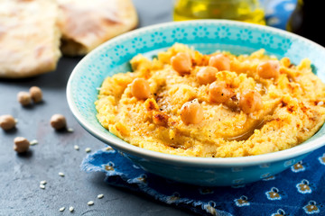 Hummus, chickpeas, with spices and pita, flat cake in a plate on a background of gray stone. Selective focus.