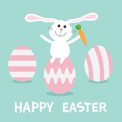Rabbit with carrot sitting on painting pink egg shell. Happy Easter bunny and three egg set. Farm animal. Cute cartoon funny character. Greeting card. Blue background. Flat design.