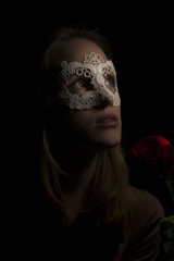 Portrait of a shy girl wearing mask and red rose on black background
