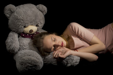 Young girl with big teddy on black background 