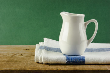 White jug and dishcloth on old wooden table over green background