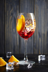 One refreshing red coctail with orange isolated on a wooden background with oranges and ice