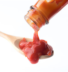 Tomato ketchup falling from bottle into spoon on white background