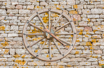 Fototapeta na wymiar réveil roue de charrette, fond mur de pierres 