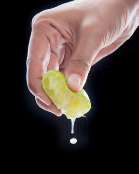 Hand squeeze lime with lime drop on black background